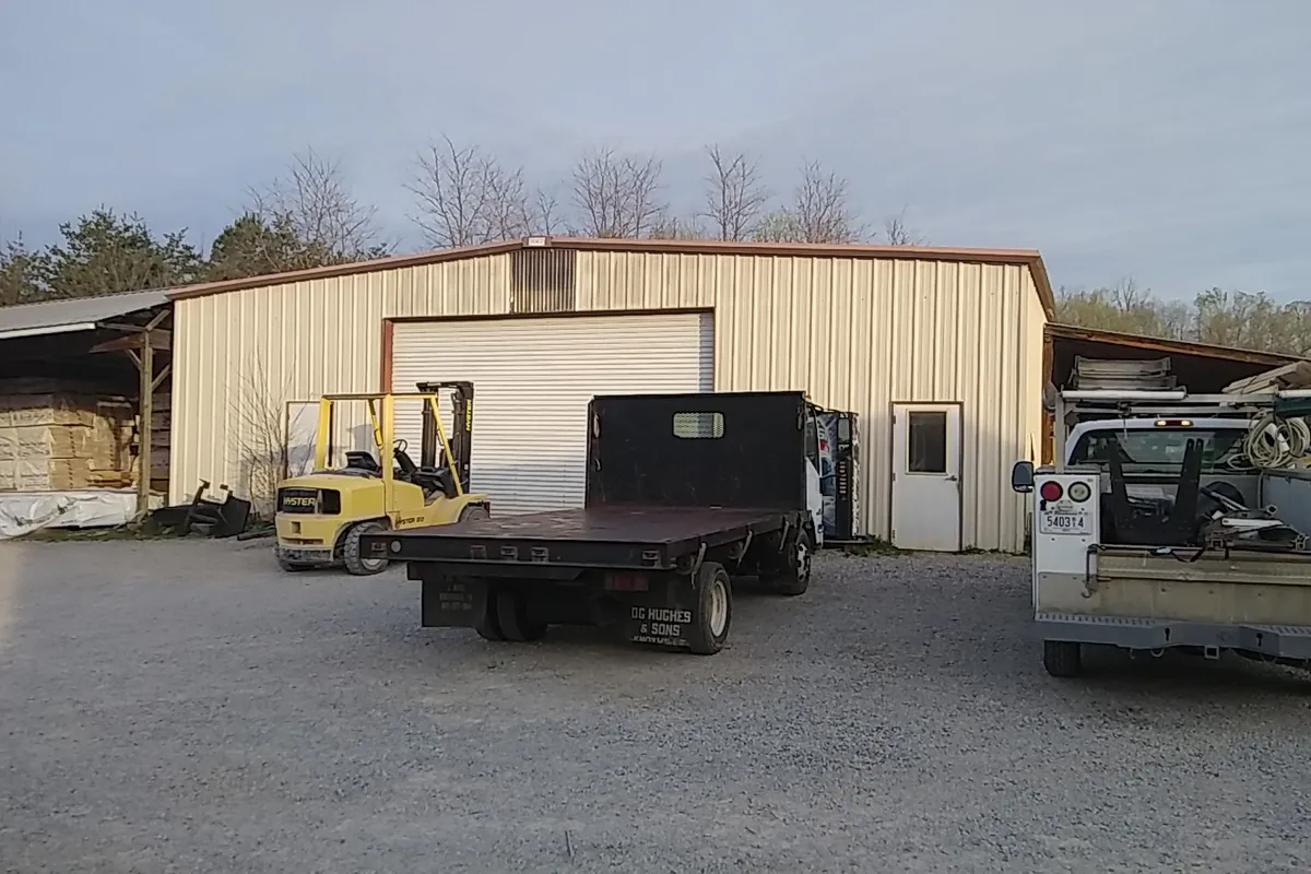 The Bivens metal shop building with a forklift, flatbed truck and covered lumber racks